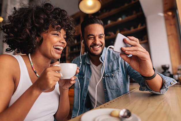 Pareja sentada sonriendo mientras ven un celular