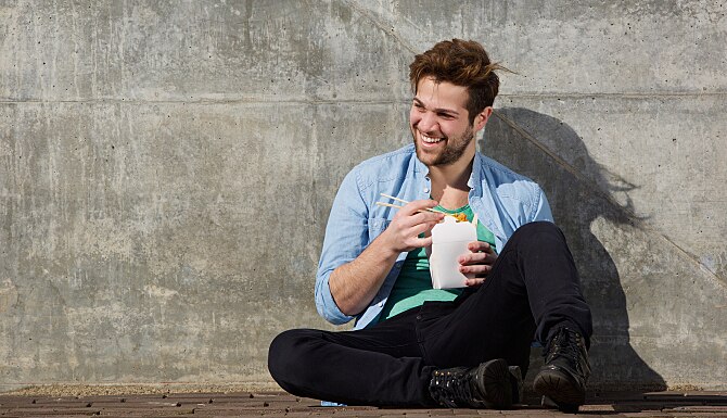 Cheerful young man eating chinese take away food with chopsticks