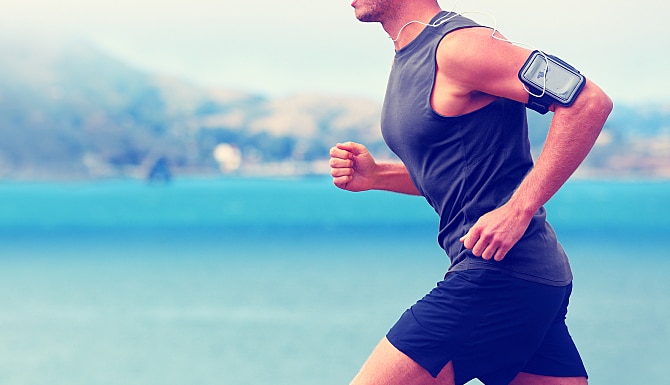 Cardio runner running listening smartphone music. Unrecognizable body jogging on ocean beach or wate Cardio runner running listening smartphone music. Unrecognizable body jogging on ocean beach or wate