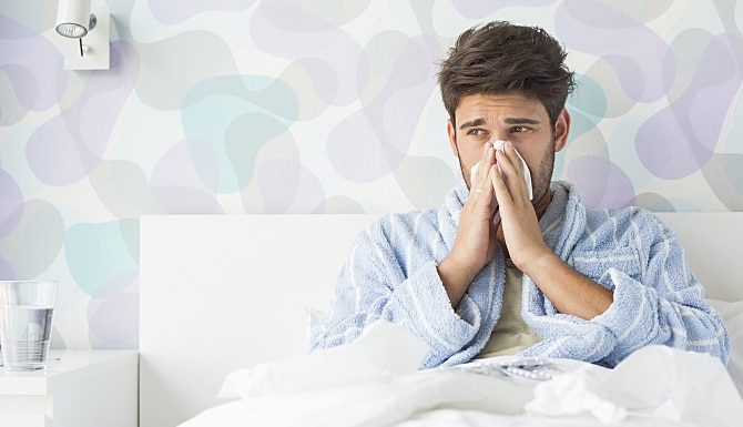 Sick man blowing his nose while sitting on bed at home Sick man blowing his nose while sitting on bed at home