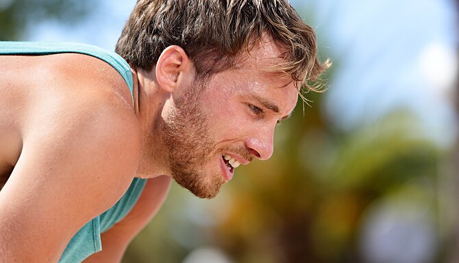 Tired exhausted man runner sweating after cardio workout. Running male adult taking a break and brea